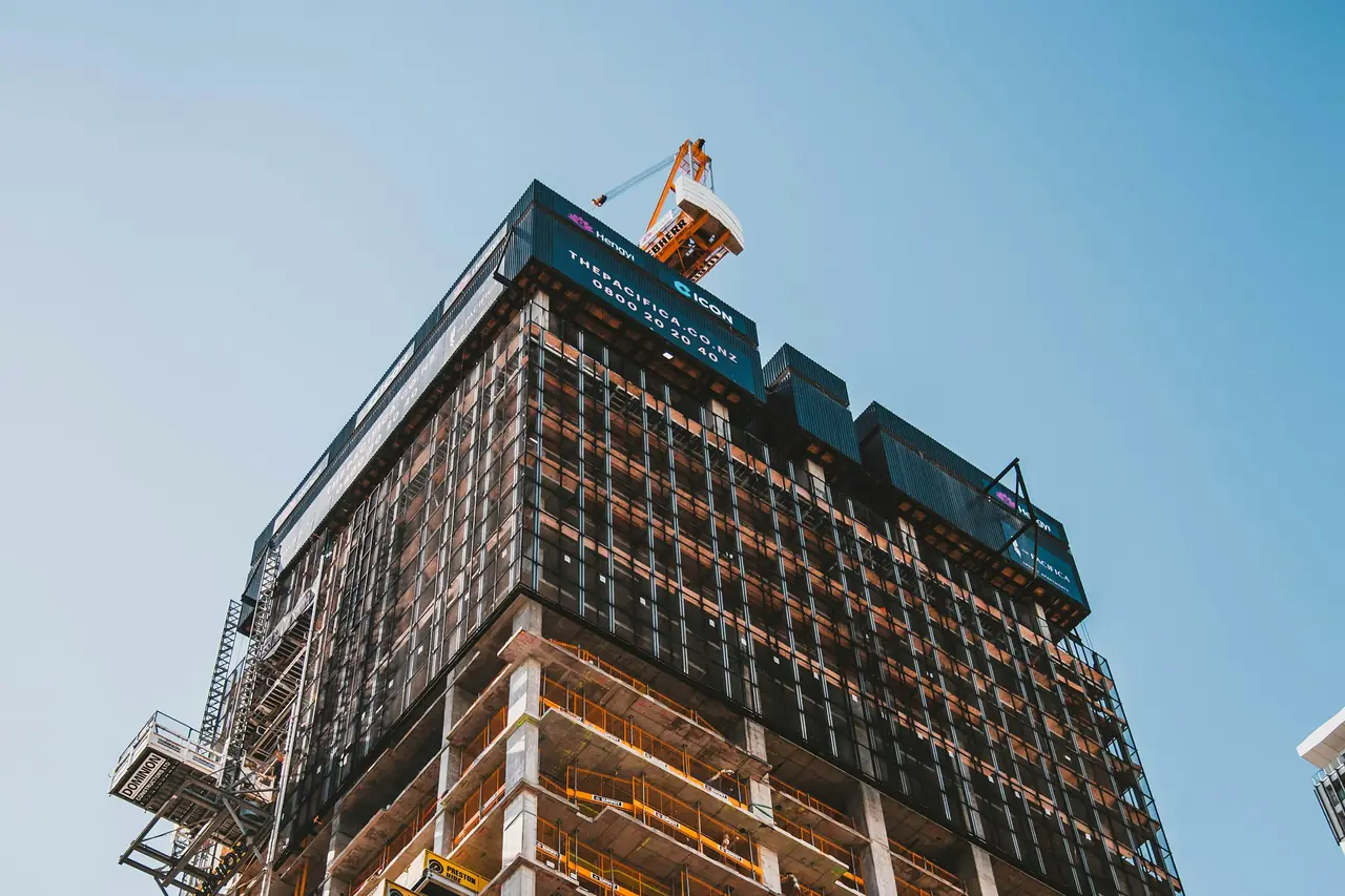 A mixed-use tower under construction at golden hour, scaffolding wrapping every completed floor.