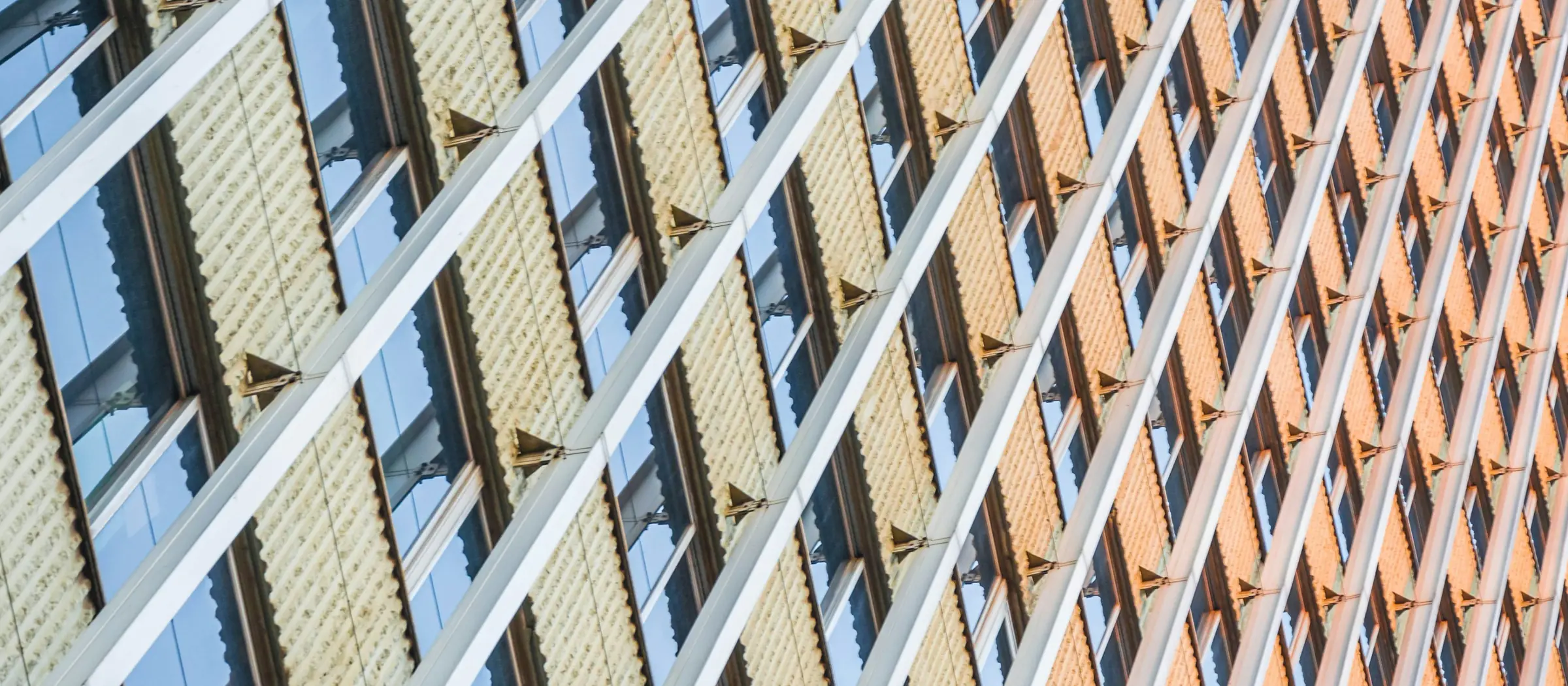 A high-rise curtain wall raking across the frame at golden hour, its glazing units repeating floor after floor.