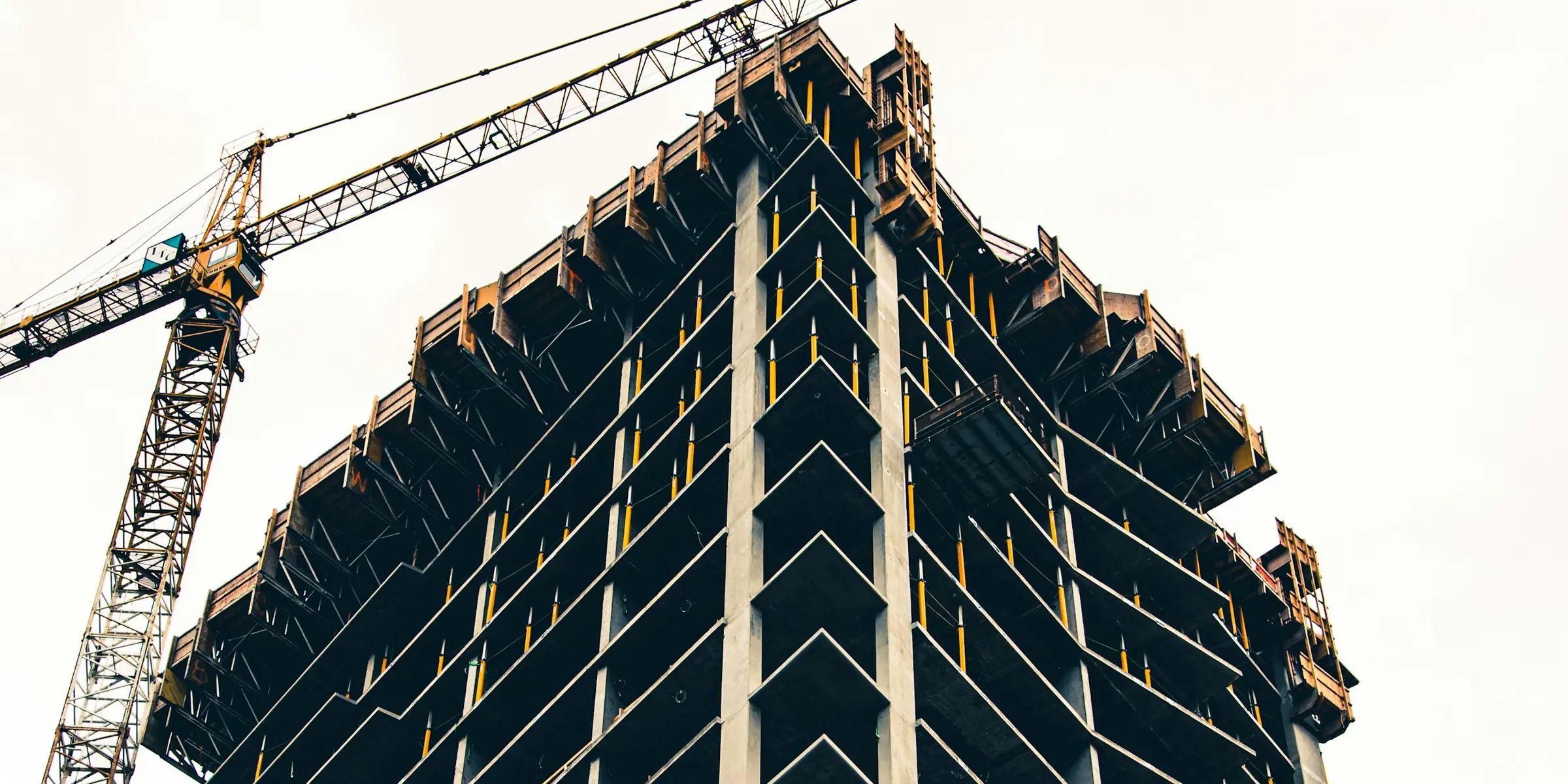 A tower still in frame, its upper floors open to the sky, a tower crane standing off its north corner.